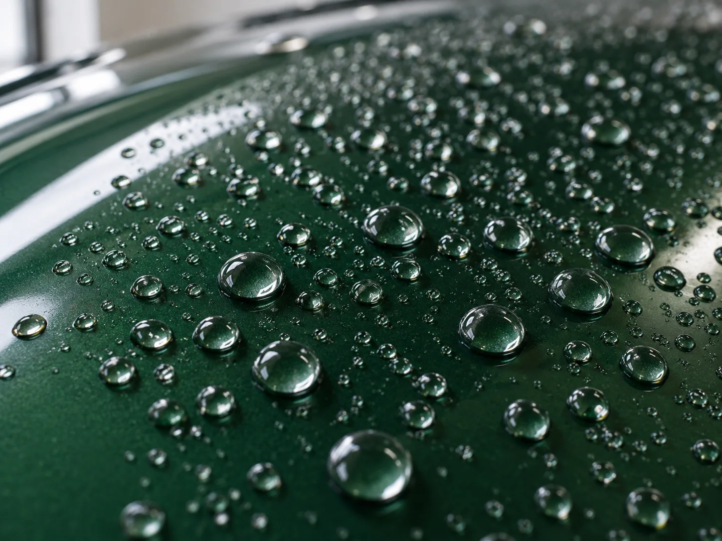 Illustrative close-up of water beading on glossy dark green automotive paint